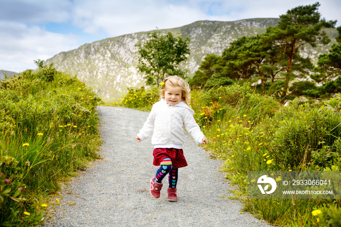 Cute little happy toddler girl running on nature path in Glenveagh national park in Ireland. Smiling and laughing baby child having fun spending family vacations in nature. Traveling with small kids