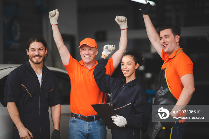 Group of young and senior male and female car mechanics in garage wearing uniform enjoying and celebrating with female worker holding clipping board