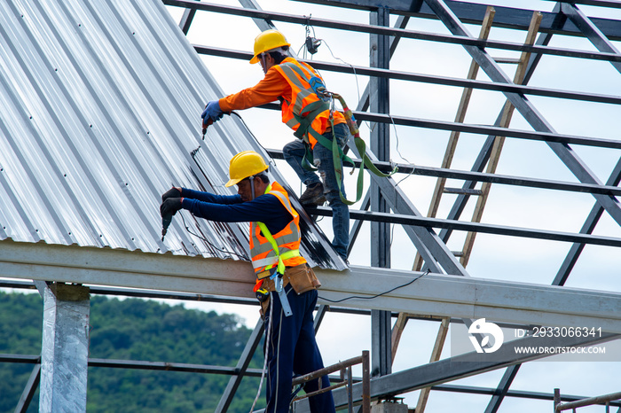 Roofer worker in protective uniform wear and gloves, using air or pneumatic nail gun and installing asphalt shingle on top of the new roof,Concept of residential building under construction.