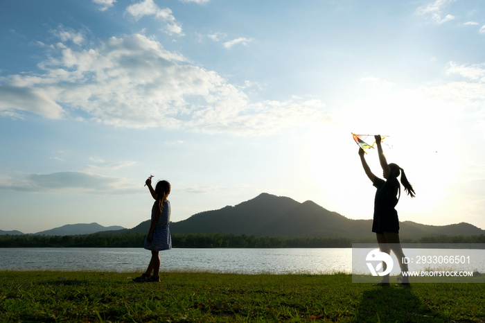 Children are flying kites while running on a meadow by the lake at sunset with their mother. Healthy summer activity for children. Funny time with family.