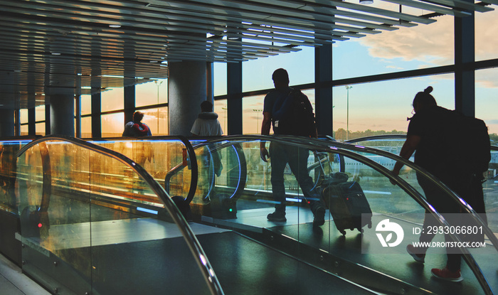 View on the aiport window with woman walking with suitcase at the departure hall during the sunset. Wide angle view with copy space.