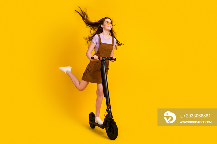 Full length body size view of attractive cheerful dreamy girl riding scooter air blowing isolated over bright yellow color background