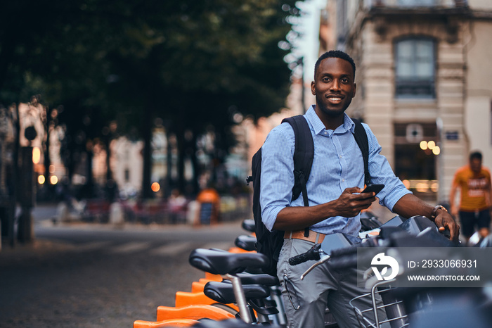 Young attractive student is renting bike and is making web payment using his mobile phone.