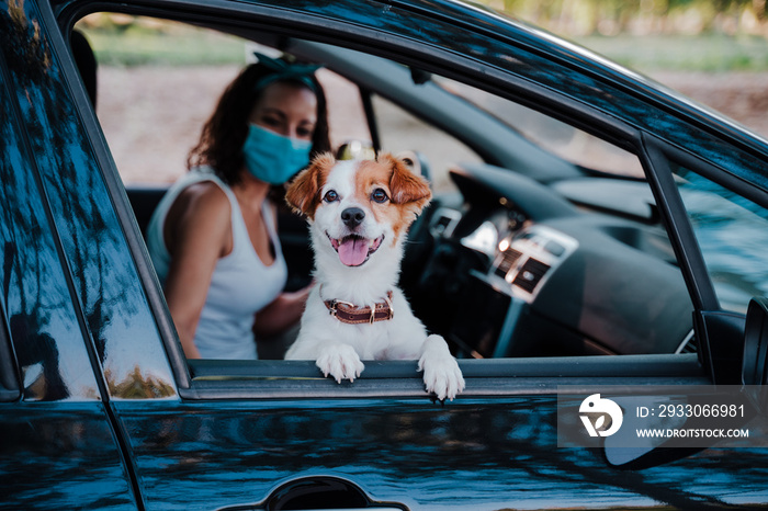 young woman wearing protective mask in a car. cute jack russell dog besides. Selective Focus on dog. Travel and new normal concept