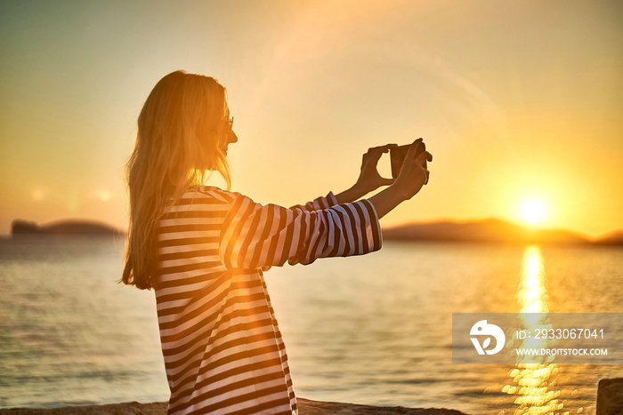 Woman traveler tourist using smartphone, taking photo of sea view at sunset in summer day. Enjoying European, Famous popular touristic place in world.