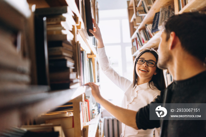 people, knowledge, education and school concept - happy student girl and the guy choose books in the old library