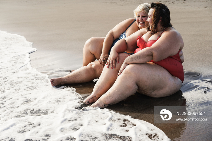 Plus size women sitting on the beach having fun during summer vacation - Focus on right face