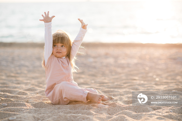 Happy funny little child 2-3 year old playing at beach over sea at background in sun light outdoors. Small kid wearing summer clothes outside. Vacation season. Childhood.