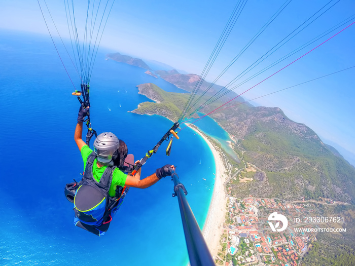 Paragliding in the sky. Paraglider tandem flying over the sea with blue water and mountains in bright sunny day. Aerial view of paraglider and Blue Lagoon in Oludeniz, Turkey. Extreme sport. Landscape