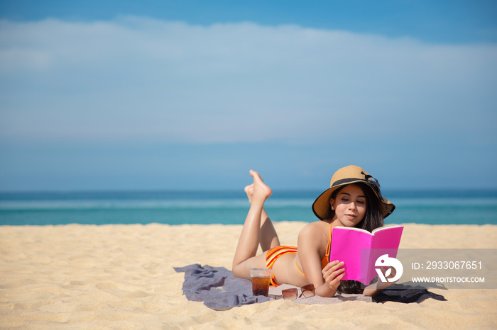 An Asian woman takes A rest and reading a pink book on the beach While relaxing on vacation for the weekend on sunny days and nice weather in travel and holiday concept.