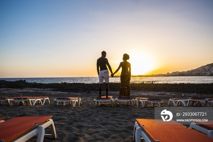 joyful and love concept for black race african couple standing at the beach and loving taking hands with a great beautiful sunset colored in front of them. enjoying the lifestyle and vacation.