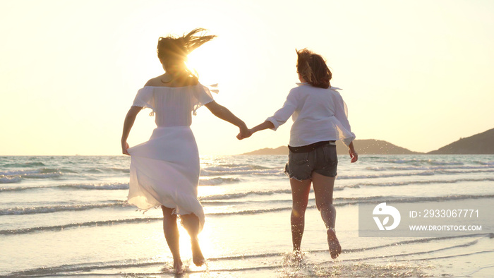 Young Asian lesbian couple running on beach. Beautiful women friends happy relax having fun on beach near sea when sunset in evening. Lifestyle lesbian couple travel on beach concept.