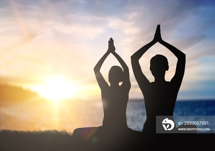 mindfulness, spirituality and outdoor yoga - silhouettes of couple meditating in lotus pose over sunset and sea background