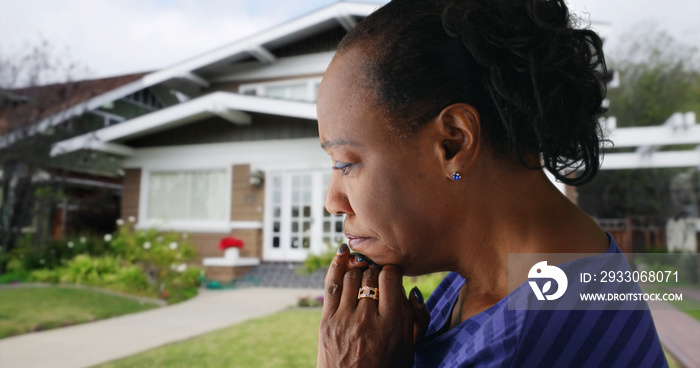 An elderly black woman prays outside her home