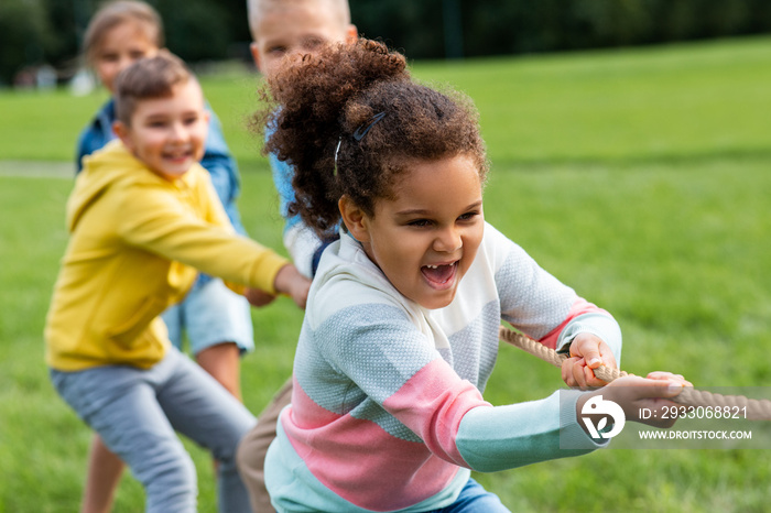 childhood, leisure and people concept - group of happy kids playing tug-of-war game and running at park