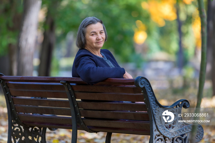 Aged woman sitting on bench in autumn park