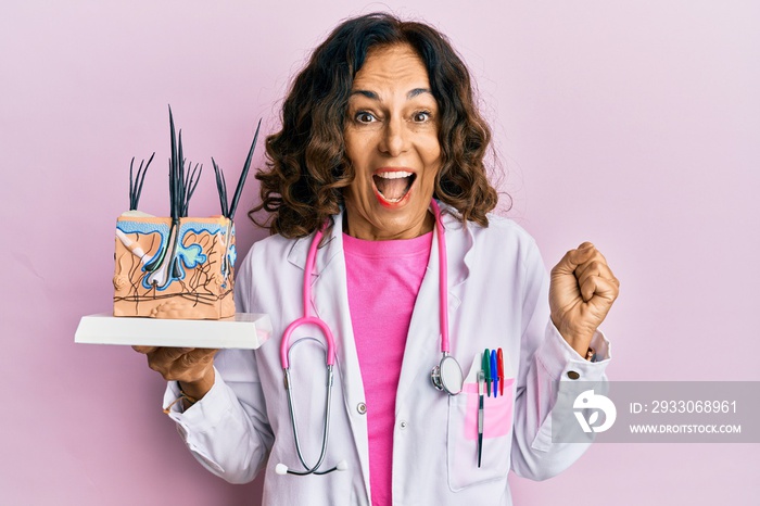 Middle age hispanic doctor woman holding model of human anatomical skin and hair screaming proud, celebrating victory and success very excited with raised arm