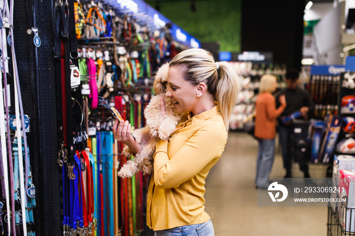 Beautiful middle aged blond woman buying accessories and food for her poodle puppy in pet shop.