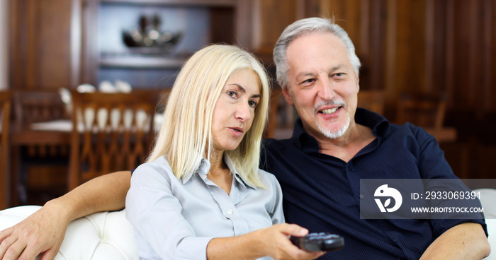 Portrait of a happy mature couple in their home watching tv together