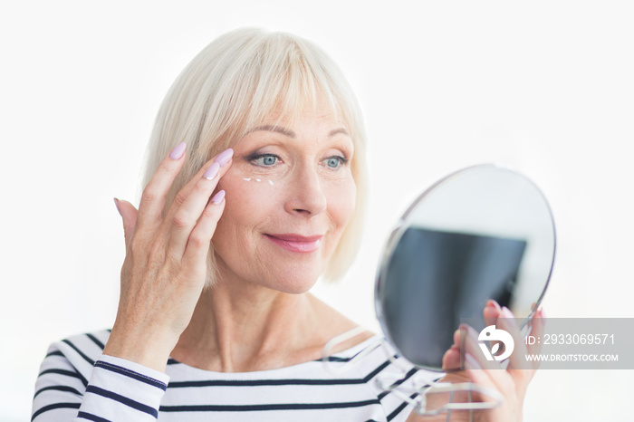 Happy senior woman applying eye anti-wrinkle cream