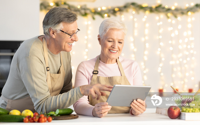 Senior Couple Using Digital Tablet Searching Christmas Recipes In Kitchen