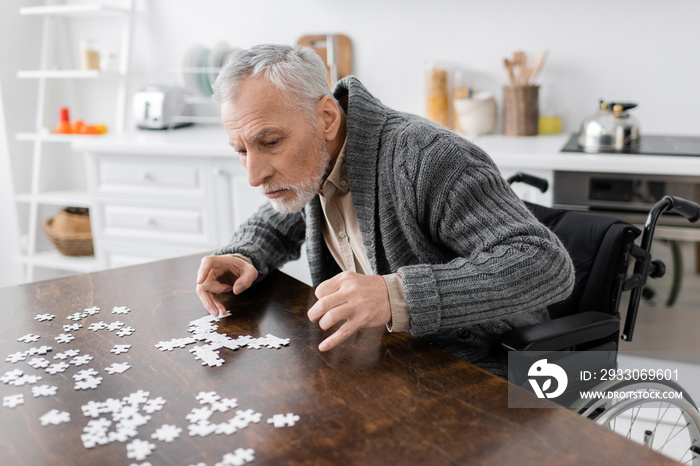 man with disability and parkinson syndrome sitting near jigsaw puzzle on table at home.