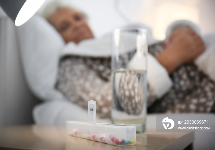 Container with pills and glass of water on table of senior woman