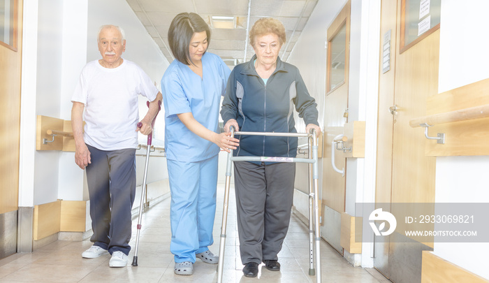 Asian doctor helping elder woman with walker and man in hospital aisle