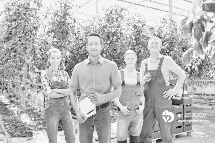 Black and white photo of Confident supervisor standing with farmers in greenhouse