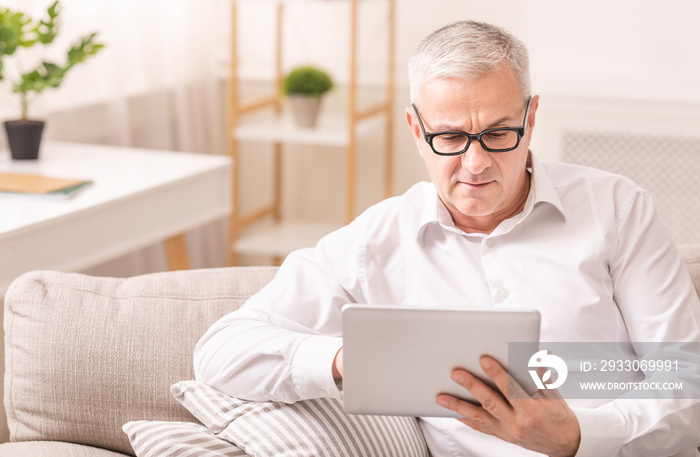 Senior man using digital tablet sitting on sofa