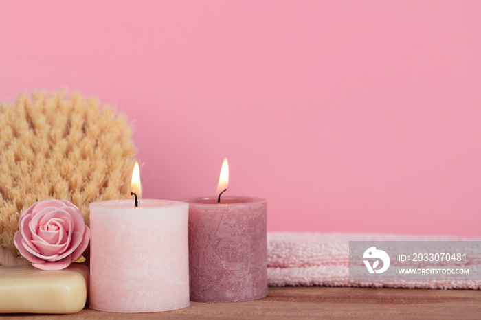 Pink spa still life with candles, towel, body brush, soap and rose on wooden desk - ready for aromatherapy and bath