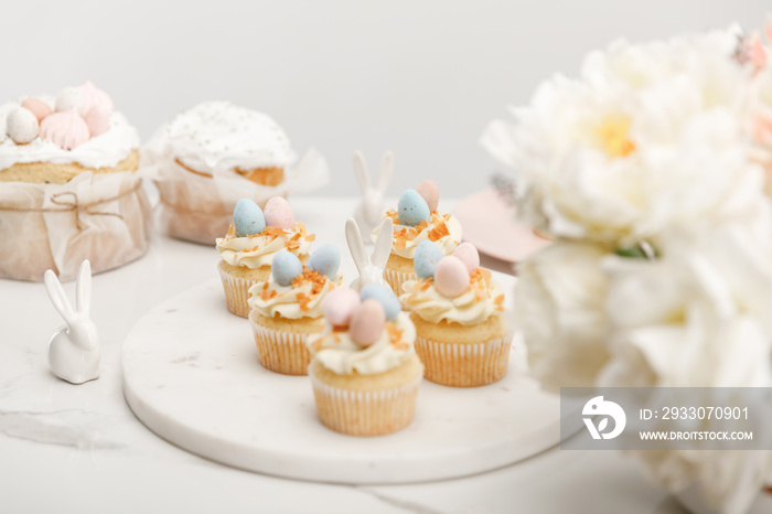 Selective focus of cupcakes with decorative bunnies on round board, flowers and easter cakes isolated on grey