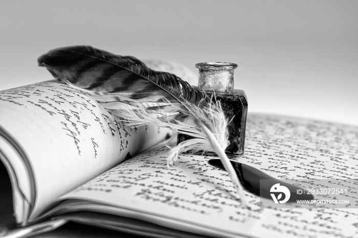 Old writing feather and ink spot with handwritten letter in background, black and white