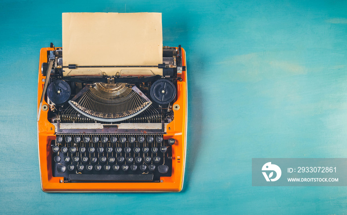 Workspace with orange vintage typewriter on blue wooden table background, toned