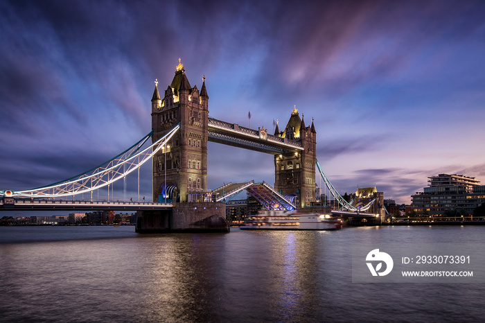 Long exposure view of the lifted Tower Bridge in London with a ship passing by during evening time