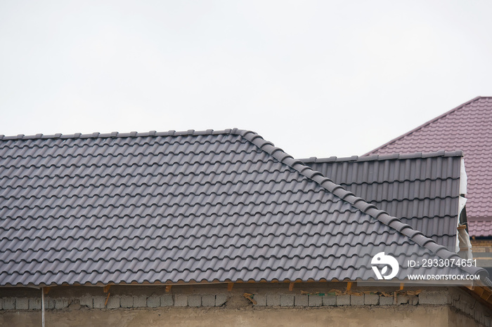 Building a house with a tiled roof. Directing wooden roof beams. Gray roof tiles and chimney of red brick. Unfinished house. Attic under the roof of the house. Round roof slope.