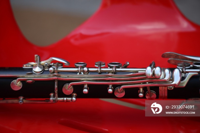 Black wooden clarinet instrument placed on red plastic chair, selectable focus.