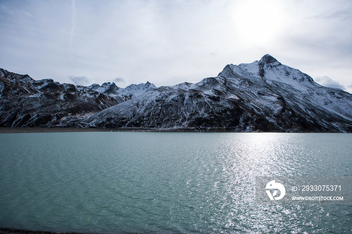 Water of a mountain lake with snowy hilltops in the background during dawn