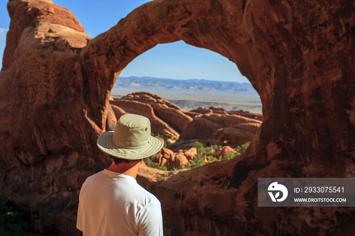 A hiker looking back through the Double-O Arch in Arches National Park, Utah.