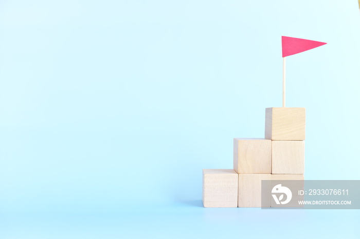 Ladder to success concept. Stacked wooden blocks staircase with red flag on top.