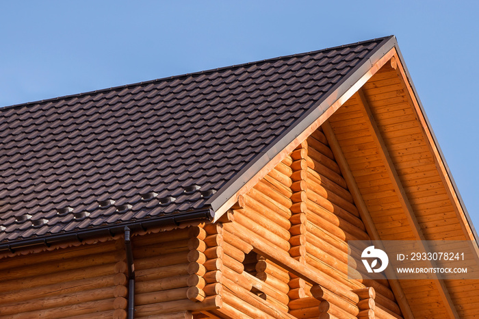 Close-up detail of new modern wooden warm ecological cottage house top with shingled brown roof and wooden sidings on blue sky background. Professionally done carpentry and construction work.