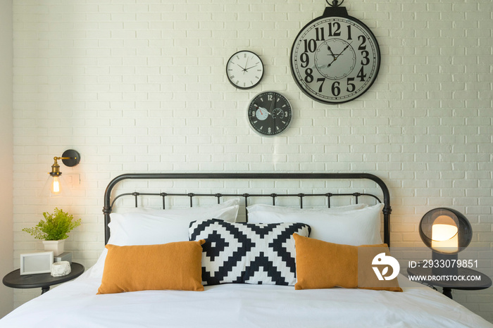 Comfortable bed with yellow and grey bedding, industrial style clock on wall.