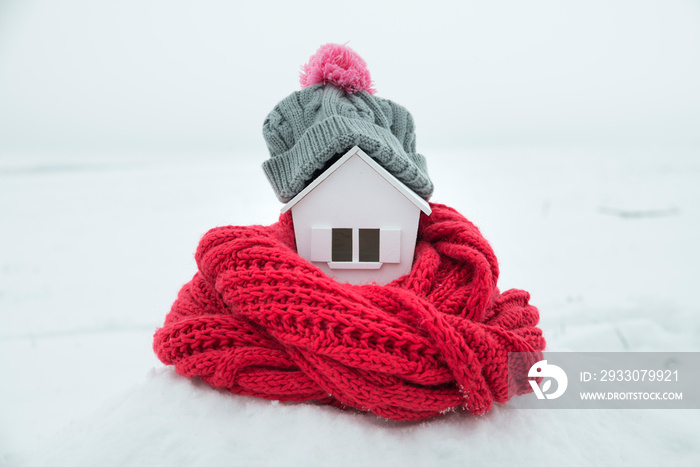 house in winter - heating system concept and cold snowy weather with model of a house wearing a knitted cap