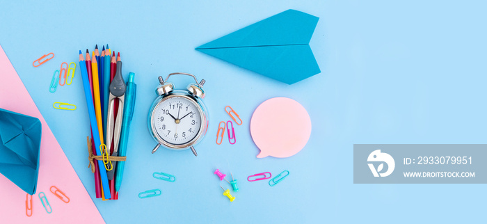 Back to school styled flat lay scene with multicolored school supplies with paper plane on pink and blue background banner