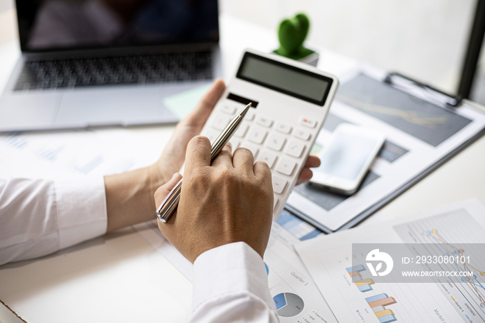 A businessman is using a white calculator to calculate financial numbers, he is sitting in his private office, the businessman examines the financial data from the corporate finance chart.