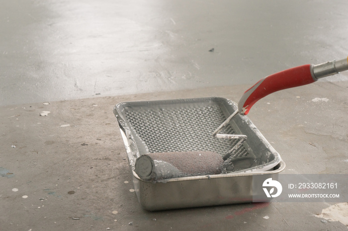 DIY professional home owner using a long handle interior paint roller and a metal tray pan to prime and seal the industrial house garage floor with specialized gray primer for longevity