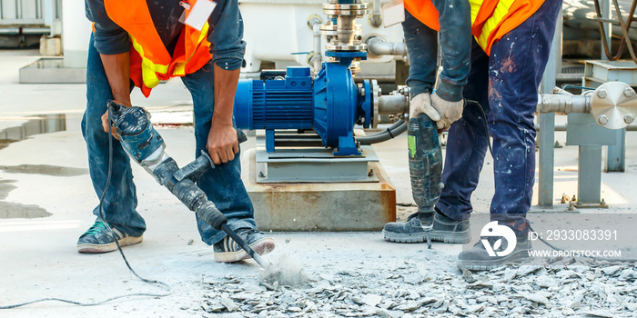 Builder worker with pneumatic hammer drill equipment breaking concrete at road construction site