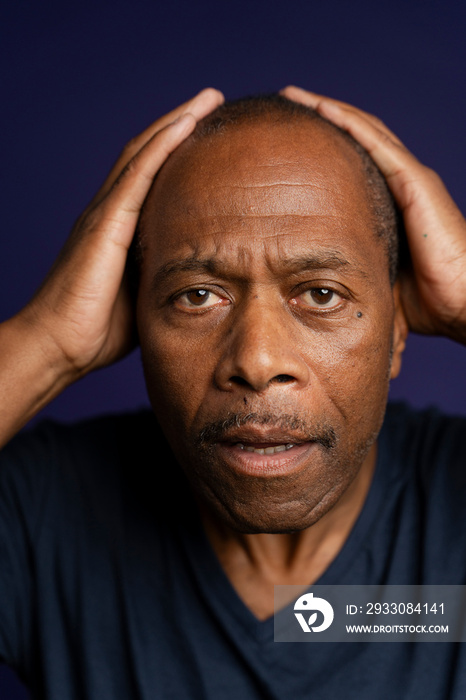 Portrait of worried man with hands on head against purple background