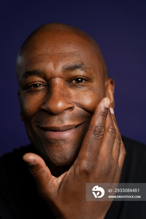 Portrait of smiling man with hand touching face against purple background