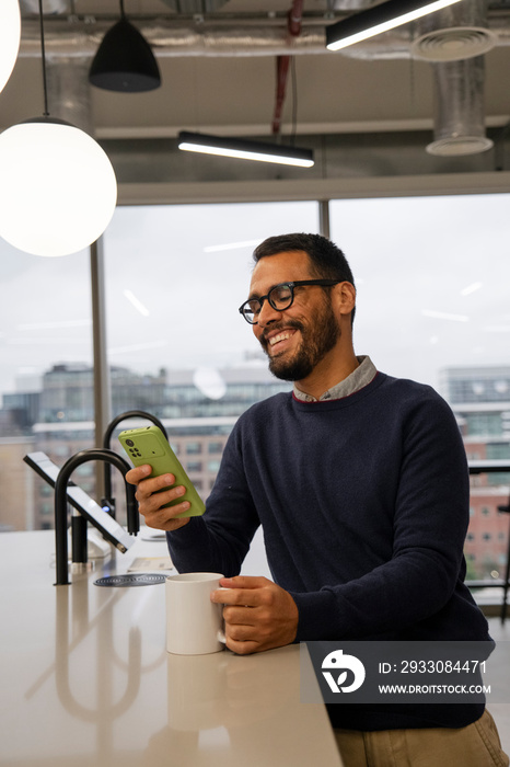 Man using smart phone in office kitchen